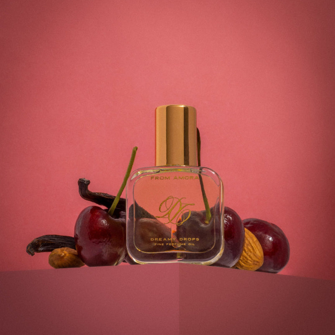 A small, clear bottle of concentrated perfume oil labeled 'Cherry Candy' with a gold cap, surrounded by cherries and other fruits on a red background.